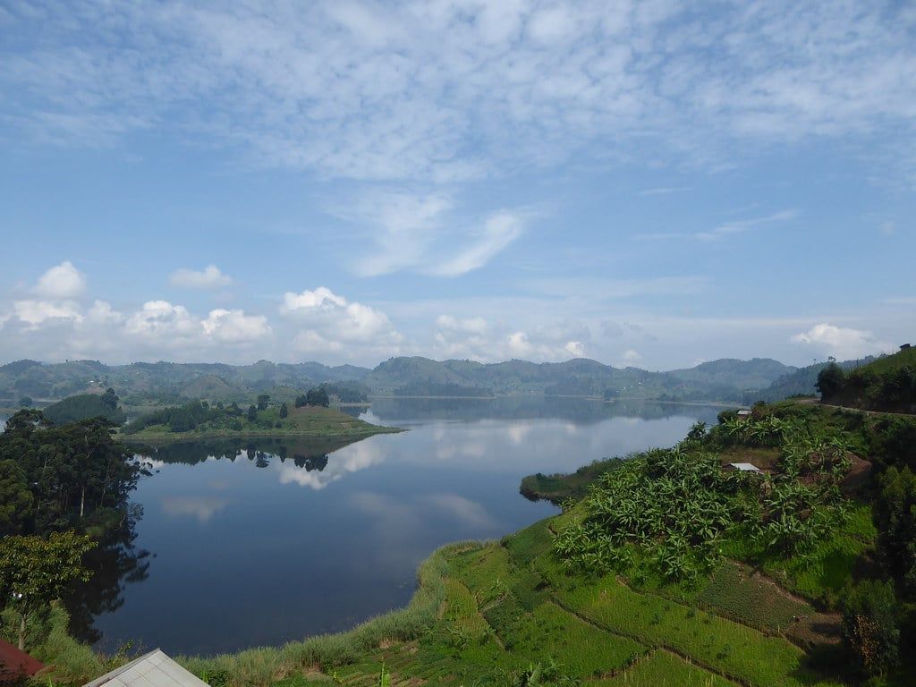 Calm waters of Lake Mutanda reflecting clouds and surrounded by green terraced hillsides near Bwindi Impenetrable National Park.
