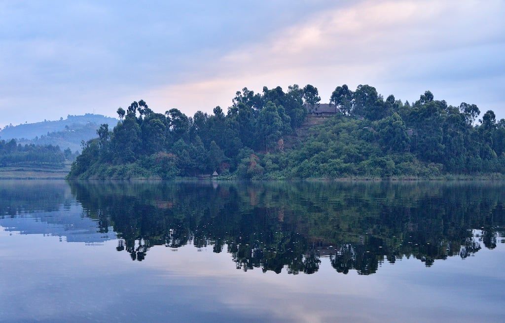 A wooded island with a hillside lodge reflects on the calm waters of Lake Bunyonyi near Bwindi Impenetrable National Park.
